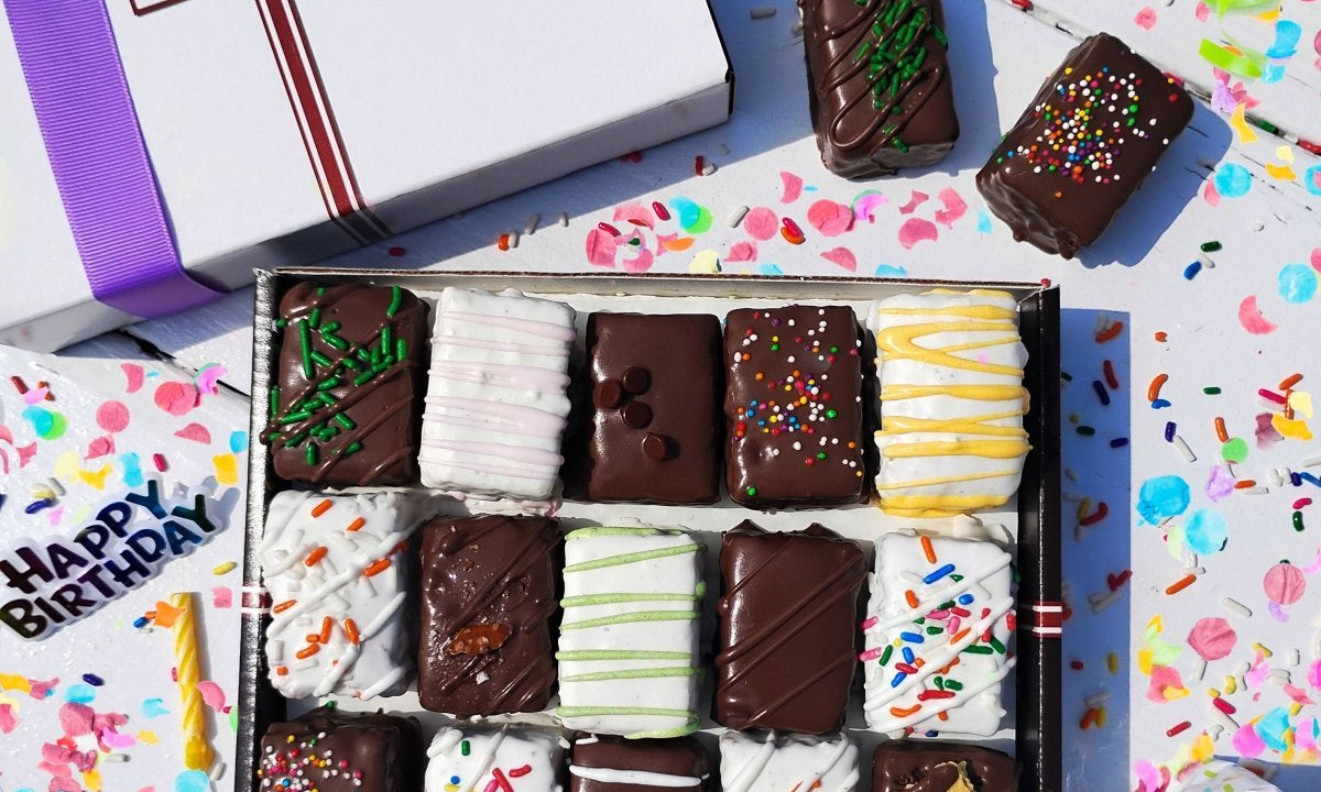A box of brownie and cake bits sitting on a white surface surrounded by birthday decorations.