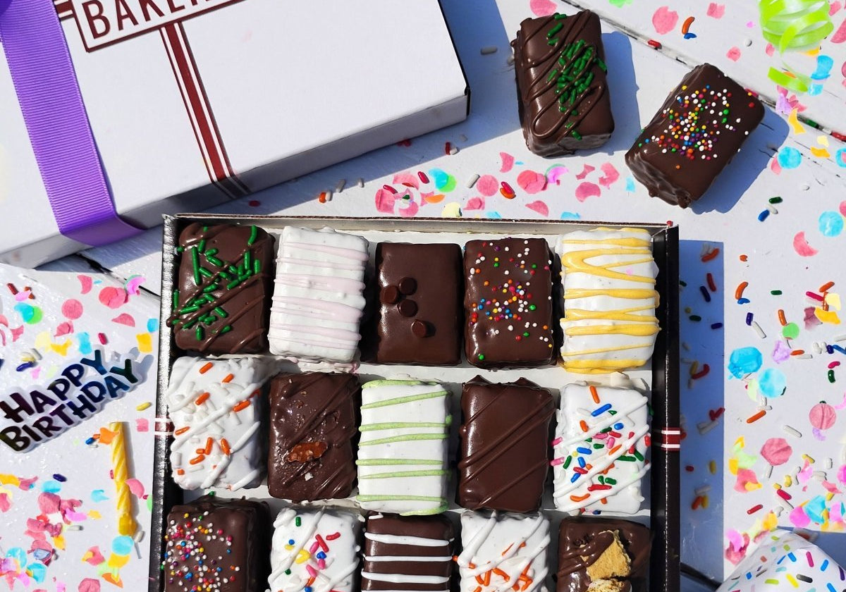 A box of brownie and cake bits sitting on a white surface surrounded by birthday decorations.