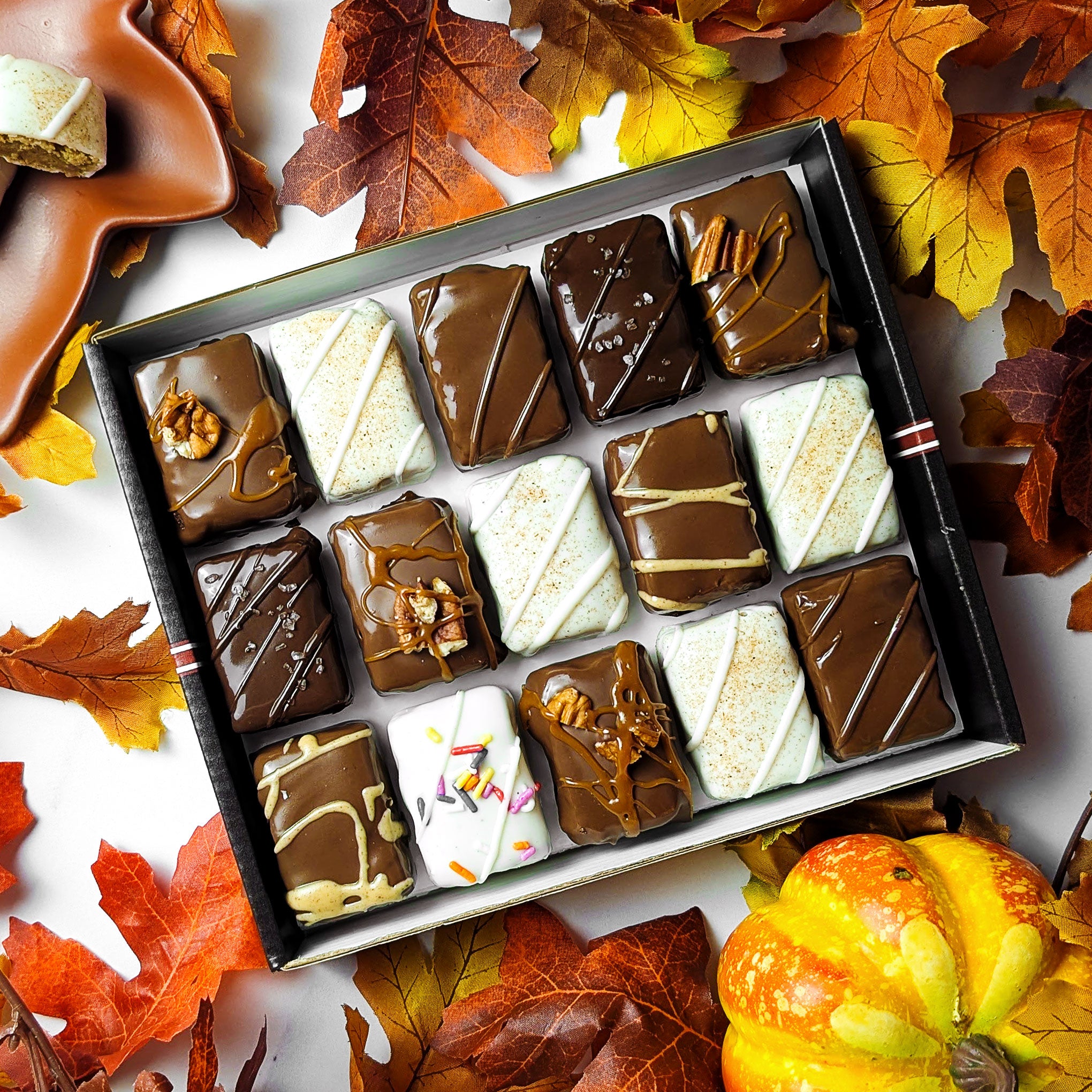 Open gift box of seasonal Fall Combo brownie and blondie bites surrounded by autumn leaves and a pumpkin, available for a limited time with nationwide shipping.