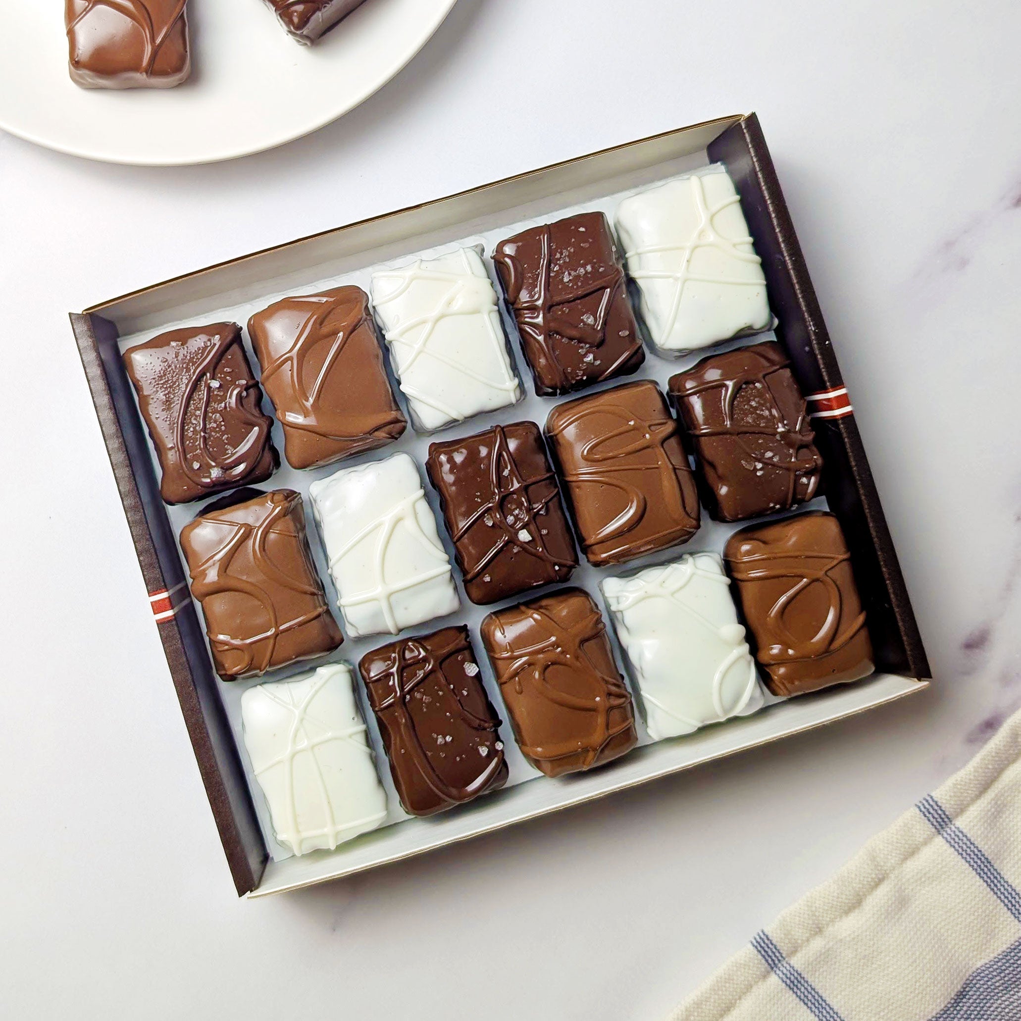 Nettie’s Bakery Gluten-Free Combo with 15 chocolate-covered brownie bites in an open gift box, plus three bites on a cream plate, photographed overhead on white marble.