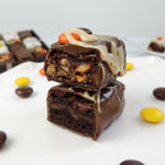 Nettie’s Bakery Reese’s Pieces Brownie Bite cut in half and stacked to reveal a fudgy brownie center with a peanut butter layer, coated in chocolate and topped with peanut butter drizzle and Reese’s Pieces—a Halloween treat available for nationwide shipping.