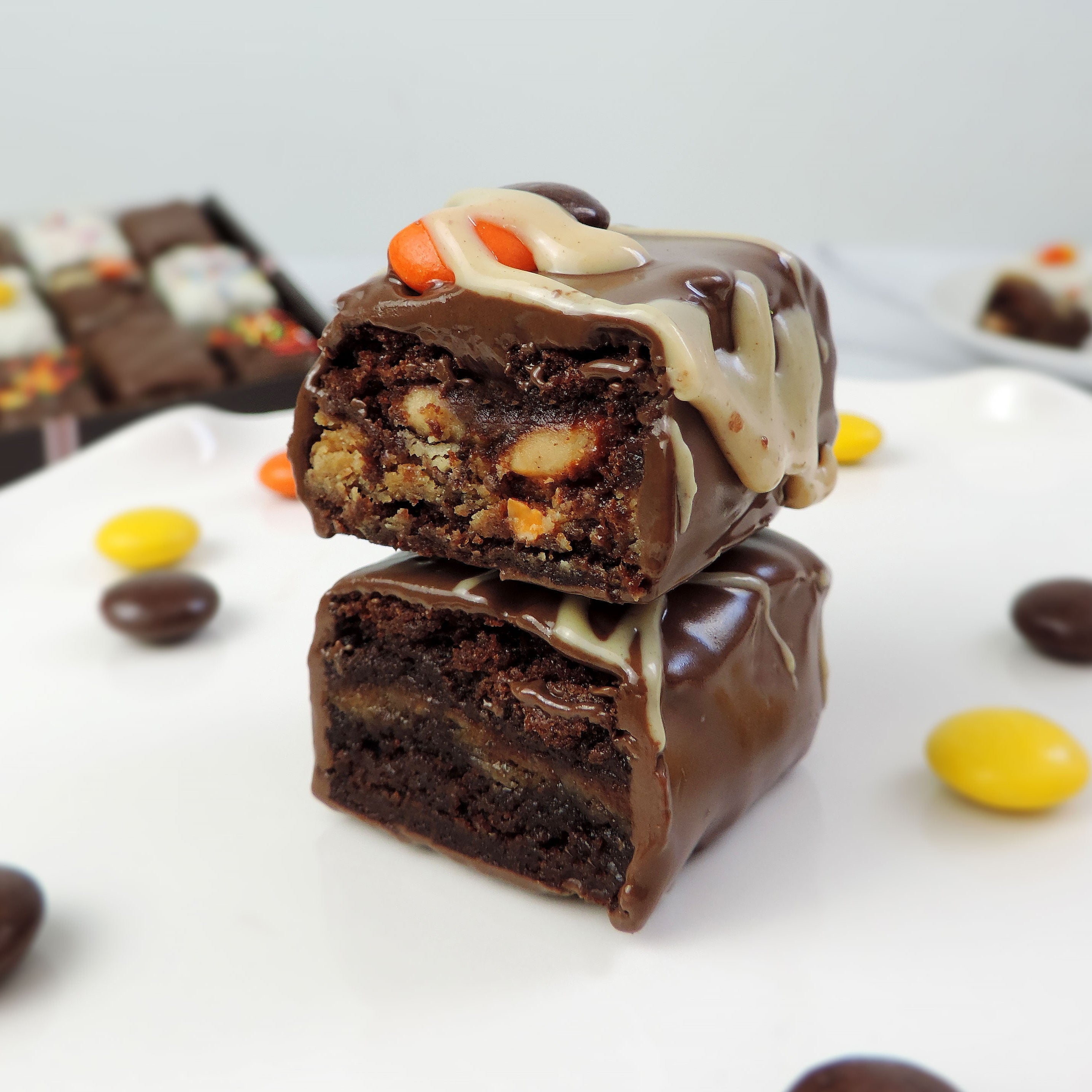 Nettie’s Bakery Reese’s Pieces Brownie Bite cut in half and stacked to reveal a fudgy brownie center with a peanut butter layer, coated in chocolate and topped with peanut butter drizzle and Reese’s Pieces—a Halloween treat available for nationwide shipping.
